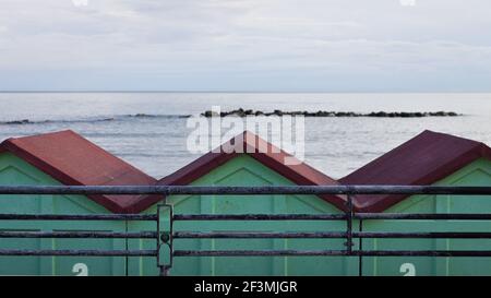 Una serie di cabine da spiaggia rosse e verdi dietro una recinzione in acciaio sulla costa mediterranea di fronte al mare (Pesaro, Italia, Europa) Foto Stock