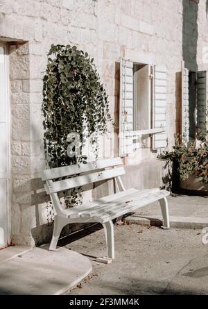 panca di legno dipinta di bianco in ombra davanti ad una casa di pietra sotto fiore in estate. Viaggi Croazia. Vista sulla strada Foto Stock