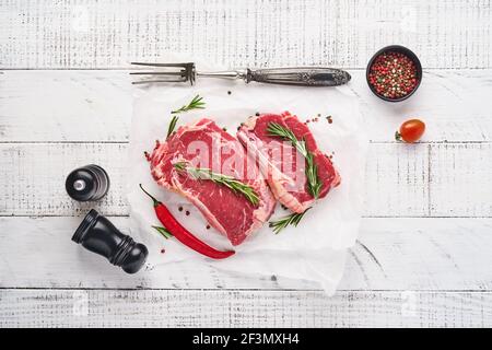 Due bistecca cruda di New York con rosmarino e spezie su un pezzo di carta pergamena su vecchio sfondo di legno bianco. Vista dall'alto. Bock up. Foto Stock