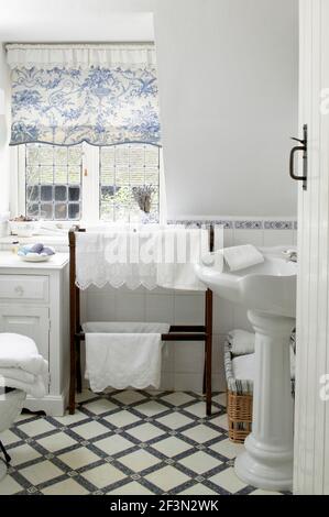 Country style traditional white bathroom with Victorian style pedestal washbasin, towel stand and tiled floor. Stock Photo