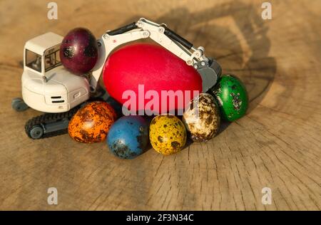 modello di un escavatore in metallo giocattolo accanto a uova grandi e piccole multicolore dai colori vivaci. Concetto di vacanza di Pasqua per le imprese di costruzione. Affari Foto Stock