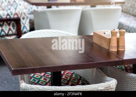 porta tovaglioli in legno con shaker per sale e pepe su un tavolo in legno di una terrazza estiva di un ristorante con sedie in vimini, primo piano tavoletta marrone vuota. Foto Stock