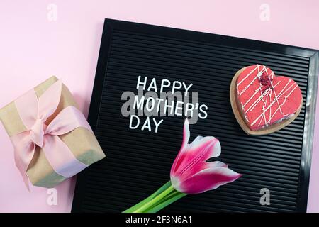 Cartellone nero con lettere bianche in plastica con citazione Happy Mothers giorno e fiore sapone, cuore su sfondo rosa. Foto Stock