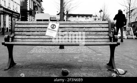 Londra UK, marzo 17 2021, sedile in legno vuoto senza persone e un cartello di avvertimento per la distanza sociale Foto Stock