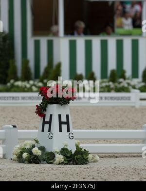 Dressage equestre con lettera H con cassa di fiori di gerani rossi in cima all'esterno dell'anello di concorso di dressage con i giudici di dressage riquadro in background Foto Stock