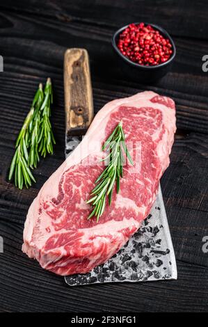 Bistecca di manzo fresca di New york Strip su un macellaio di carne sfaldante. Sfondo di legno nero. Vista dall'alto Foto Stock