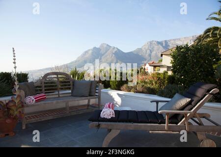 Panca in legno e lettino con cuscini e asciugamani rossi e bianchi posti sul patio con vista su Table Mountain. Foto Stock