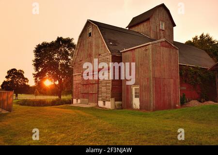 Sycamore, Illinois, Stati Uniti. Un vecchio fienile, intemperie riposa di fronte a uno di una moltitudine di tramonti che è testimoniato sulla sua esistenza. Foto Stock