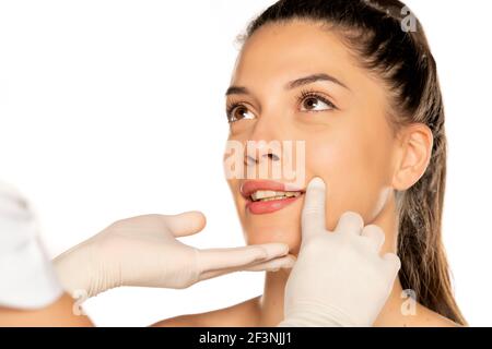 le mani del medico in guanti controlla un volto di giovane donna su sfondo bianco Foto Stock