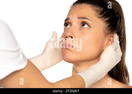 le mani del medico nei guanti controllano le orecchie dei giovani infelici donna su sfondo bianco Foto Stock