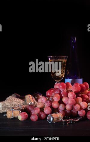 Mazzi di uve rosa e mele verdi su sfondo scuro. Un bicchiere di champagne è sullo sfondo. Vita morta. Cestino vitaminico. Spazio di copia. Foto Stock