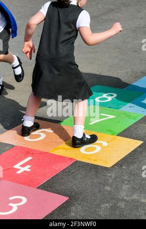 Bambino della scuola elementare che gioca a hopscotch in un parco giochi scolastico durante la pausa dalle lezioni in classe. Foto Stock