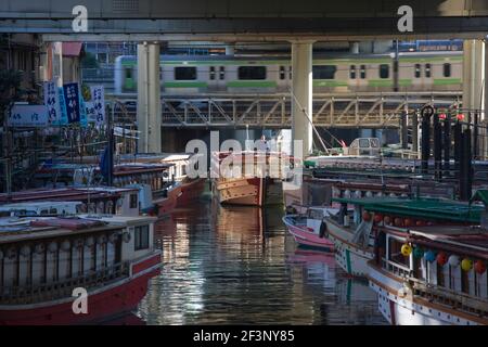 Con un treno urbano che scorre sullo sfondo, un capitano della barca facilita la sua escursione yakatabune houseboat passato altri ormeggiati in una stretta cana Foto Stock