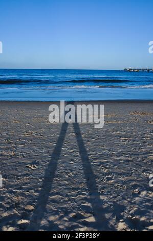 La spiaggia di Usedom durante un umore serale. Il sole che tramonta crea una lunga ombra umana Foto Stock