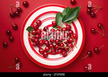 Ciliegie fresche con foglie su un piatto a strisce rosse Foto Stock