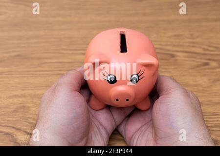 mani che tengono una banca di piggy di creta nella forma di un maiale rosa in concetto di risparmio ed economia Foto Stock