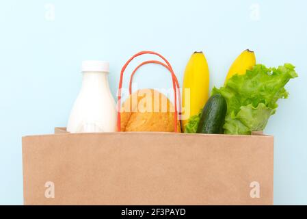 Sacchetto di carta con cibo: Foglie verdi di insalata, pane, bottiglia di latte, cetriolo, banana. Stendere su sfondo blu, vista dall'alto Foto Stock