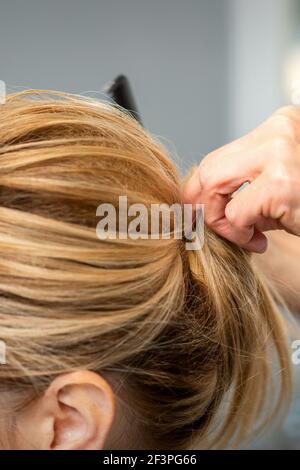 Primo piano di mani di donna parrucchiere styling capelli di una donna bionda in un parrucchiere Foto Stock