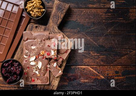Barretta artigianale di cioccolato al latte con nocciole, arachidi, mirtilli rossi e lamponi secchi congelati. Sfondo di legno scuro. Vista dall'alto. Spazio di copia Foto Stock