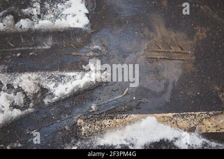 Tracce di pneumatici nella neve che si scioglie sullo sfondo di un punto di petrolio su strada asfaltata Foto Stock