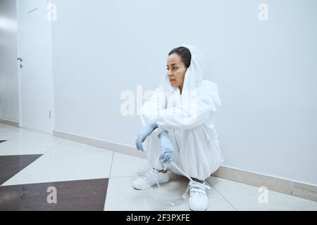 Femmina giovane medico in uniforme seduta nel corridoio e. riposo dopo il funzionamento in ospedale Foto Stock