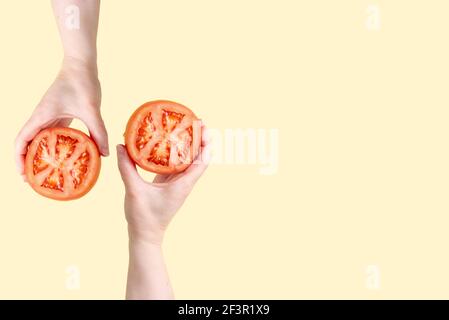 Due mani femminili che tengono metà del pomodoro in mano sullo sfondo giallo, concetto di cibo sano, primo piano. Foto Stock