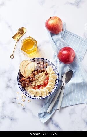 Porridge d'avena con mele caramellate con cannella, banana, fragole grattugiate e miele su sfondo di marmo chiaro, vista dall'alto. Foto Stock