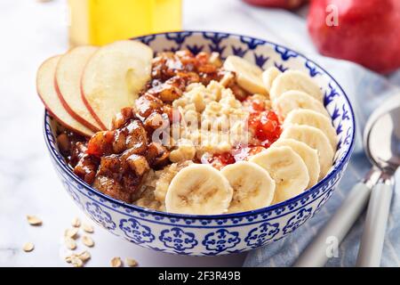 Porridge d'avena con mele caramellate con cannella, banana, fragole grattugiate e miele su sfondo di marmo chiaro, primo piano Foto Stock