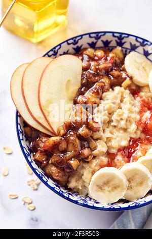 Porridge d'avena con mele caramellate con cannella, banana, fragole grattugiate e miele su sfondo di marmo chiaro, primo piano Foto Stock