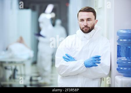 Ritratto di medico maschile maturo in uniforme guardando la macchina fotografica mentre si è in piedi nel corridoio dell'ospedale Foto Stock