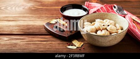 Gnocchi ripieni di carne, pelmeni, ravioli, gnocchi. Gnocchi di carne di pelmeni tradizionali russi fatti in casa con panna acida su sfondo di legno. Foto Stock