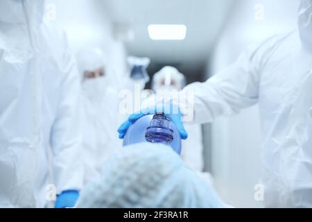 Primo piano del medico in uniforme protettiva che mette maschera di ossigeno il viso del paziente prima dell'uso Foto Stock