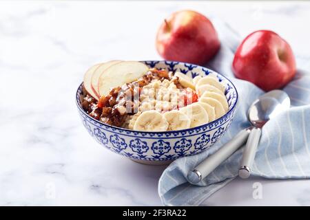 Porridge di farinata d'avena con mele caramellate alla cannella, banana, fragole grattugiate su leggero sfondo marmoreo Foto Stock