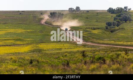 Un'auto si muove lungo una collina, lungo una strada di campagna, lasciando dietro una nuvola di polvere Foto Stock