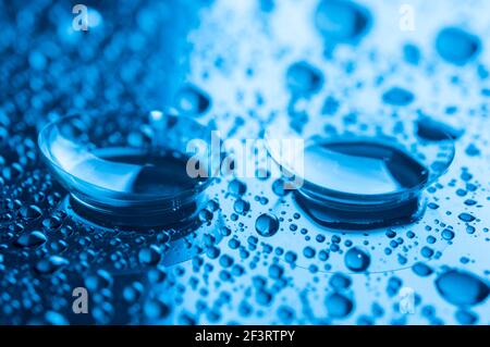 Primo piano di due lenti a contatto con gocce su sfondo scuro. Immagine con tonalità blu. Foto Stock