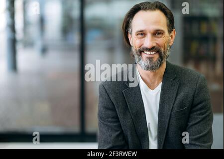 Ritratto di un bel lavoratore o amministratore delegato. Uomo caucasico di media età con un'elegante e sicura giacca formale e una t-shirt bianca sorride e guarda direttamente nella fotocamera Foto Stock