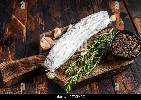 Salame spagnolo secco salchichon su un tagliere. Sfondo di legno scuro. Vista dall'alto Foto Stock