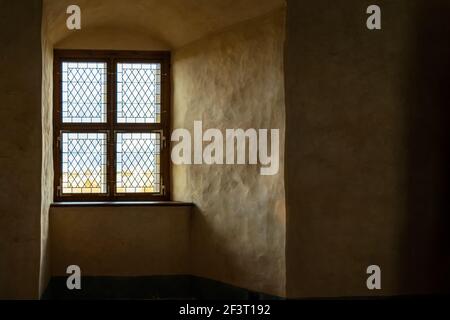 Attenua la luce che attraversa la finestra in vetro colorato in una nicchia di pareti spesse nel castello medievale Foto Stock