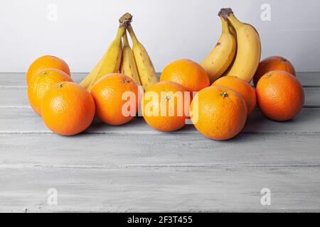 Vista delle arance e delle banane allineate su un grigio tabella su sfondo bianco Foto Stock