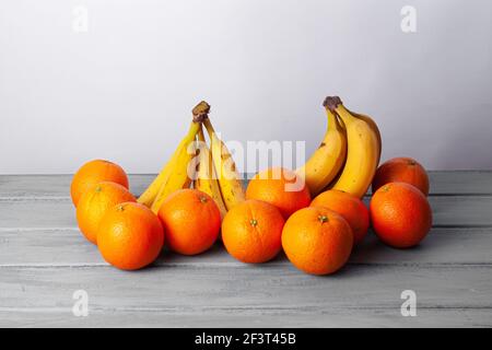 Vista delle arance e delle banane allineate su un grigio tabella su sfondo bianco Foto Stock