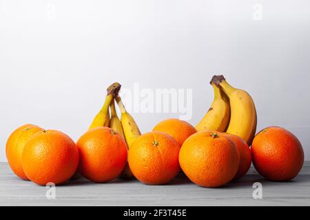 Vista delle arance e delle banane allineate su un grigio tabella su sfondo bianco Foto Stock