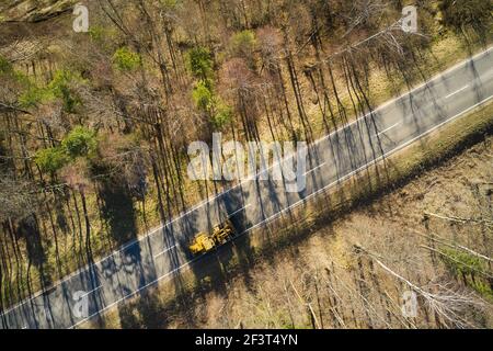 Vista aerea della strada con un trattore nella foresta autunnale. Catturato dall'alto con un drone. Foto Stock