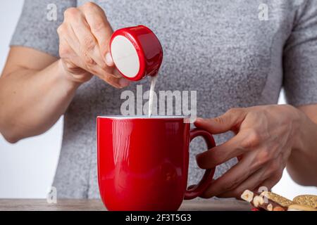 un concetto di tempo del tè o del caffè con biscotti sandwich, barrette di tazza di ceramica estetica al cioccolato e piatti, nonché una mini caraffa crematrice su legnoso Foto Stock