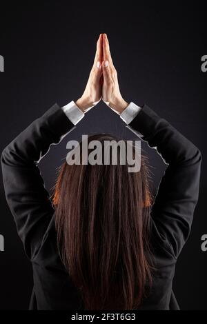 Bordo illuminato, dietro la vista della testa di una giovane donna caucasica business con capelli marroni indossare giacca e camicia su sfondo scuro.le sue mani si incontrano Foto Stock