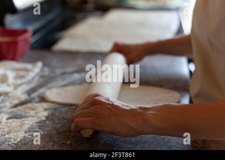 Una donna caucasica sta usando un perno di rotolamento americano per rotolare sopra gli impasti del pane per appiattirli e modellarli. Autentico sfondo cucina fatta in casa pane ma Foto Stock