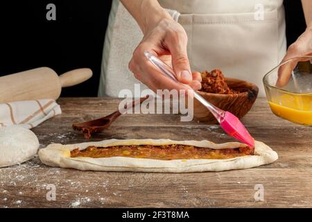 Primo piano immagine di una donna che sparge uova grezze omogeneizzate sopra la ricetta di kimali turchi come un condimento. Utilizza una spazzola rosa in silicone per alimenti Foto Stock