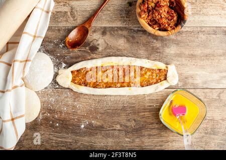 Immagine piatta che mostra una pide kimalica pronta per cuocere, una sorta di pizza turca o pane piatto con manzo macinato e uova. Impasti, recipiente per miscela, omog Foto Stock