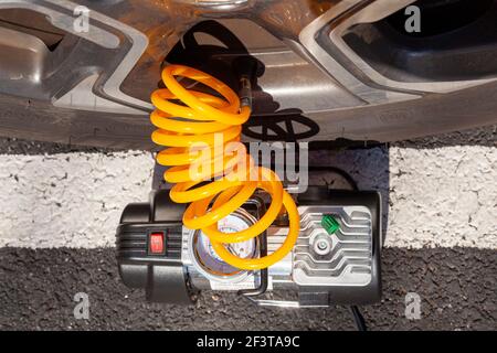 Primo piano immagine vista dall'alto di un piccolo compressore d'aria da 12 V collegato alla valvola dello stelo di un pneumatico per auto per controllare la pressione degli pneumatici e riempirlo secondo necessità. Simp Foto Stock