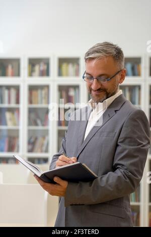 Bel Maestro maschio con gli occhiali che scrivono nel notebook. Scrittura del dirigente di affari. Uomini d'affari che hanno una penna e che scrivono una nota in un notebook. Foto Stock