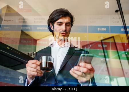 L'uomo d'affari lavora dallo smartphone mentre beve un caffè a casa Foto Stock